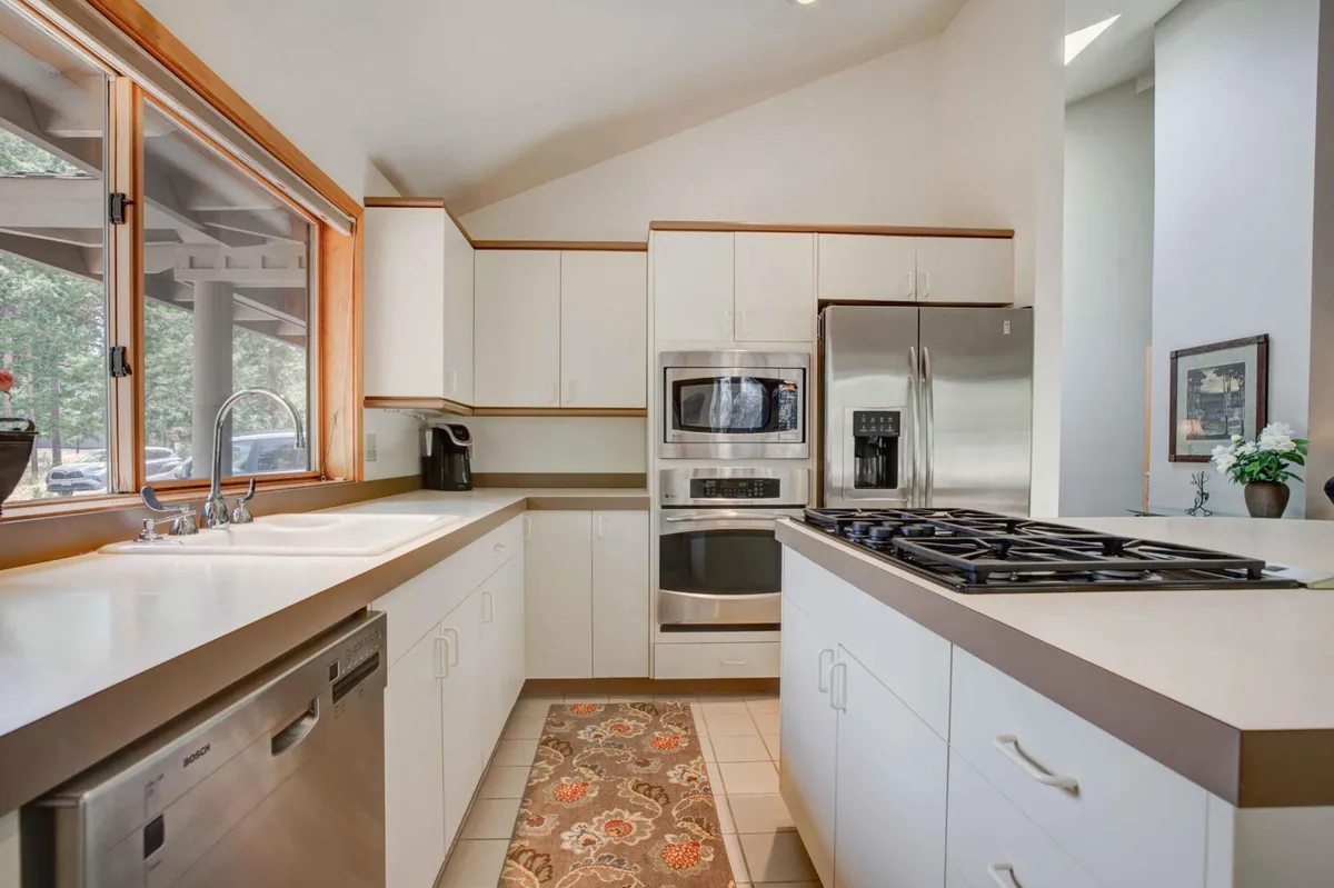This image captures a modern kitchen with a sleek kitchen island at the center, surrounded by high-end stainless steel appliances like a gas stove and dishwasher. The island features seating, inviting casual conversation or morning coffee, and the space is filled with natural light streaming through large windows.