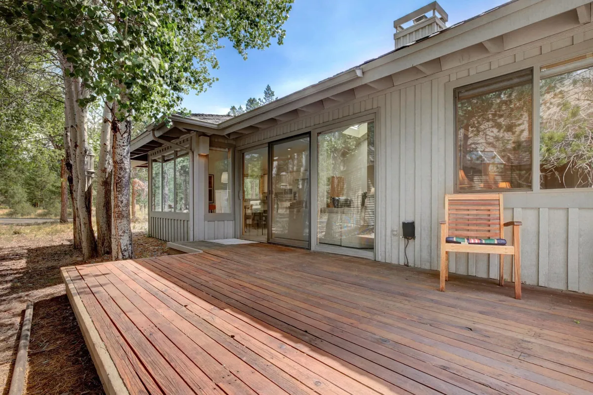 A wooden deck framed by large glass doors, surrounded by dense trees. There is an outdoor chair placed to take in the scenery, and the space invites quiet moments with nature, perfect for morning coffee or evening relaxation.