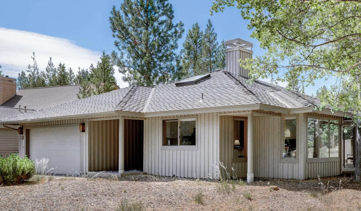 A welcoming front porch with large windows looks out onto natural surroundings, including mature trees and open space perfect for family gatherings or relaxing after outdoor adventures. The scene exudes the charm of a retreat nestled in nature, inviting families to step outside and explore.