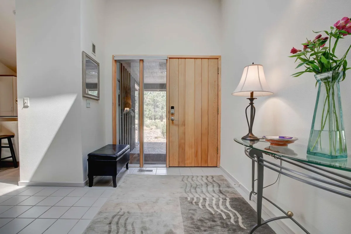 A bright, inviting entryway with a wooden front door, console table, decorative flowers, and a rug illuminated by natural light. The space exudes warmth and hospitality, offering the perfect first impression for guests returning from a day of activities.