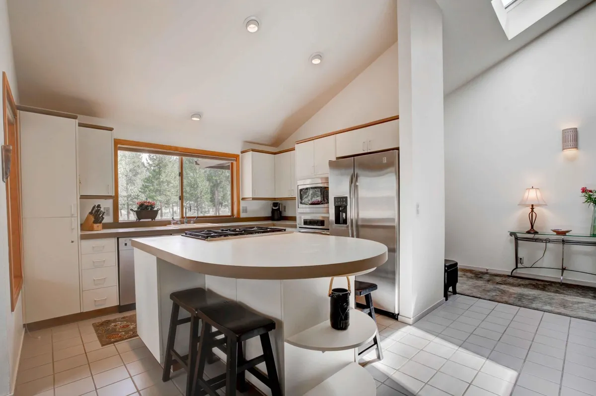 A contemporary kitchen dominated by a central island, high-end stainless steel appliances, large window, and stylish lighting fixtures. The setting is staged for cooking and socializing, with room for entertaining guests or gathering for casual meals.