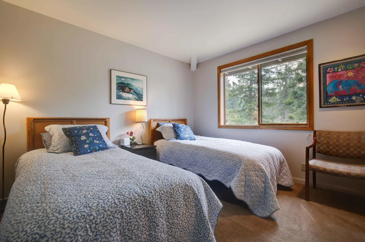 A cozy bedroom designed for comfort, featuring two twin beds, a bedside lamp, a window with a view of nature, and decorative wall art. The space feels welcoming and is ideal for guests or children looking for a restful night's sleep.